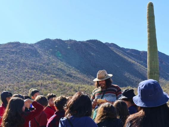 group leader speaking to a group of kids, mountain scape and sahuaro as a backdrop